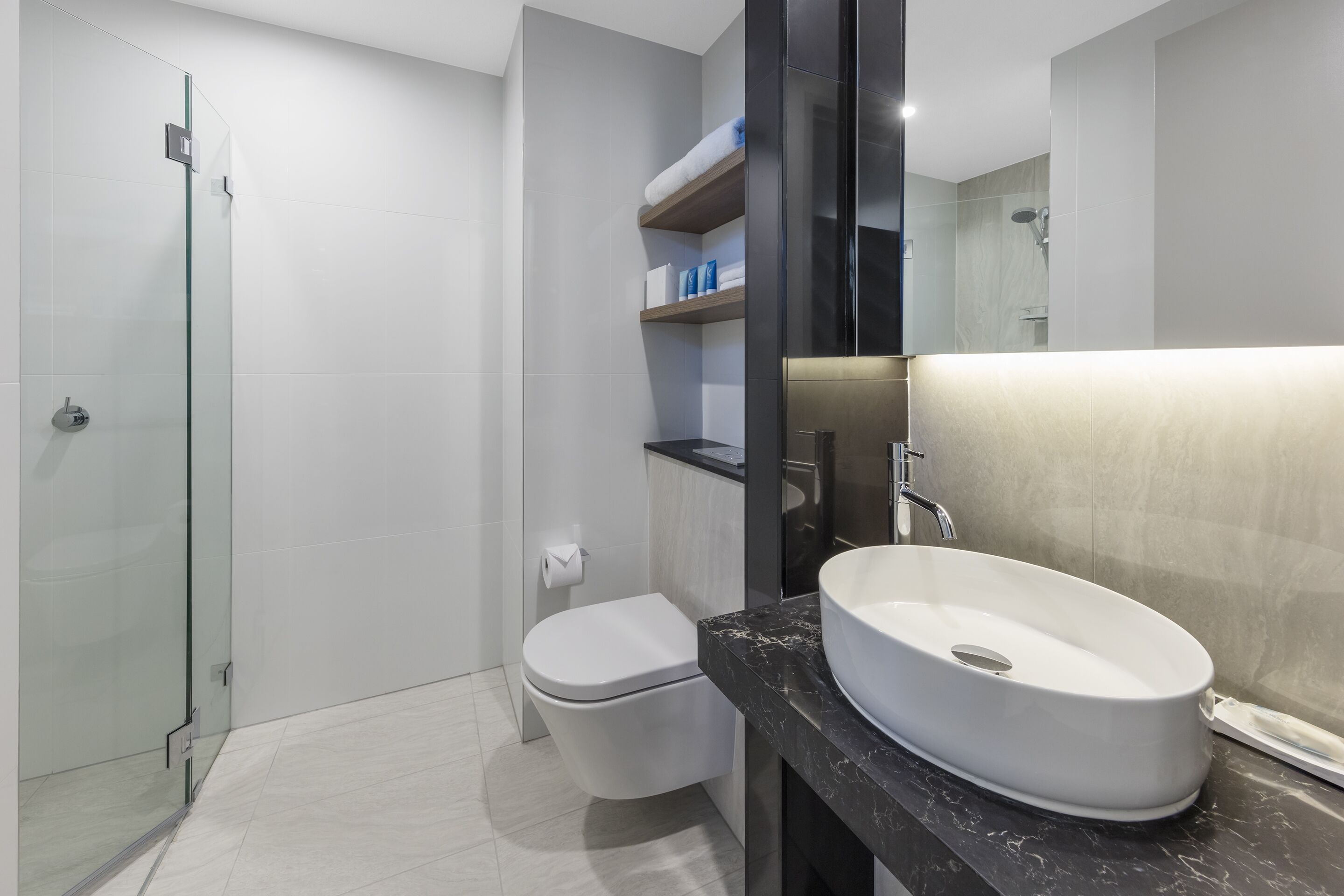 A modern bathroom with a glass shower enclosure, a white toilet, a vanity with a white sink, and a mirror.