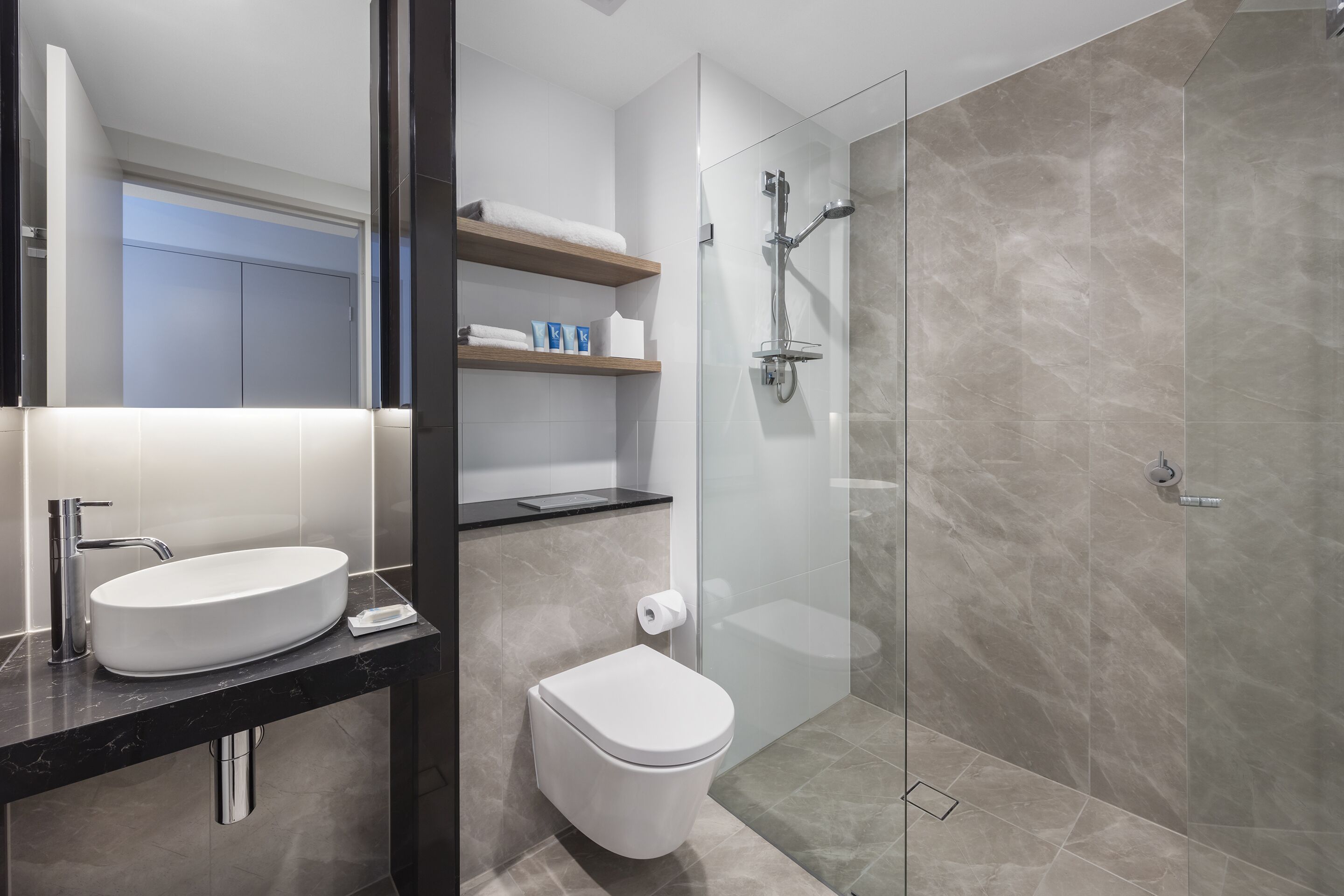 A modern bathroom with a double sink, toilet, and glass-enclosed shower.