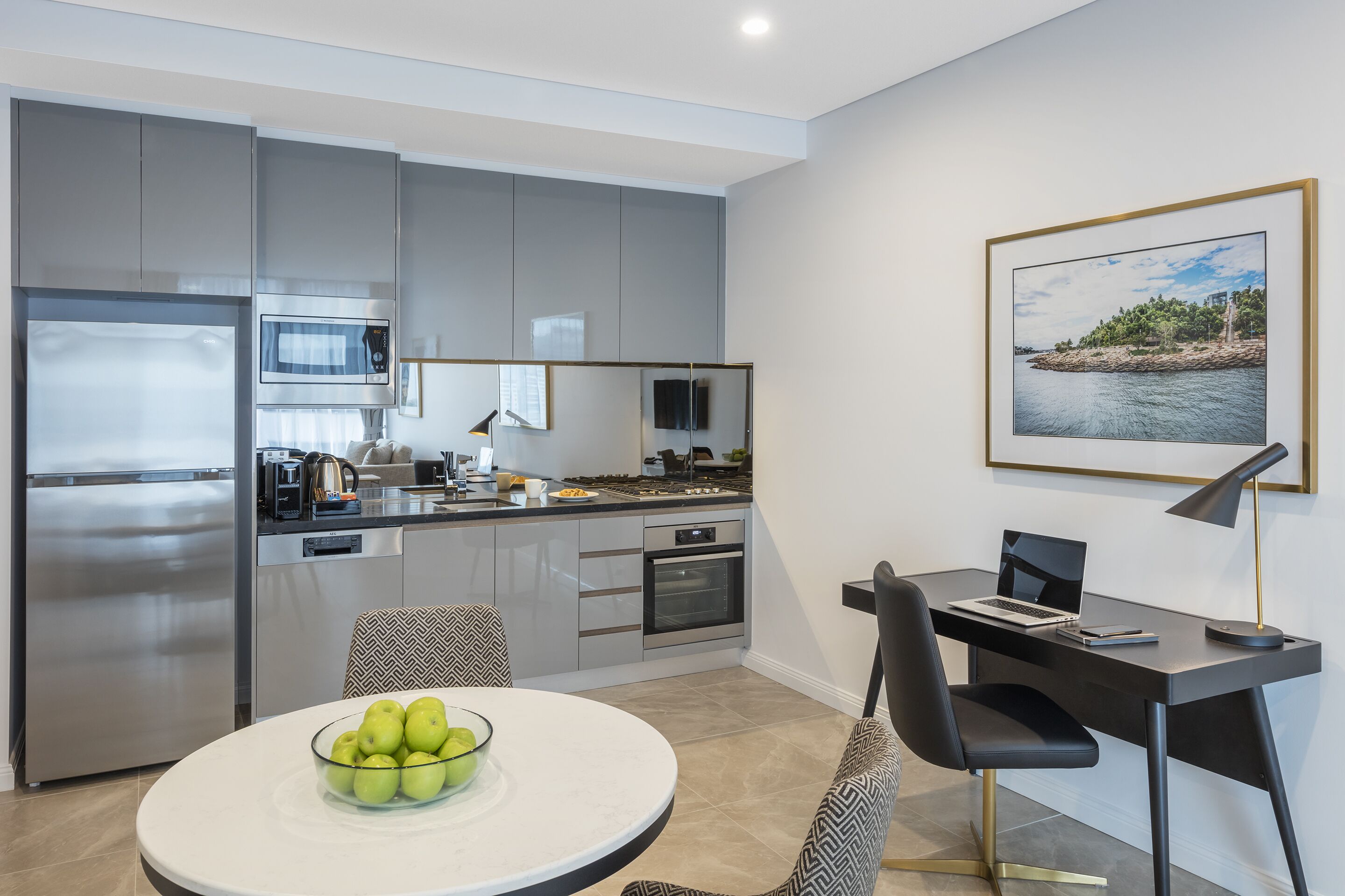 Une cuisine moderne avec des meubles gris, un réfrigérateur en acier inoxydable et un coin repas comprenant une table et des chaises.