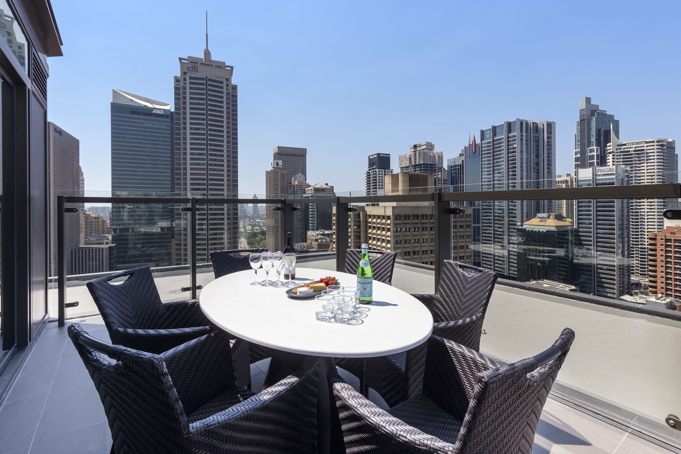 A rooftop terrace with a round table and wicker chairs, overlooking a city skyline.