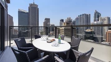 A rooftop terrace with a round table and wicker chairs, overlooking a city skyline.