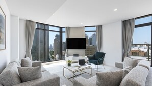 Un soggiorno moderno con divani grigi, un tavolino, un televisore a schermo piatto e ampie finestre con vista sulla città.