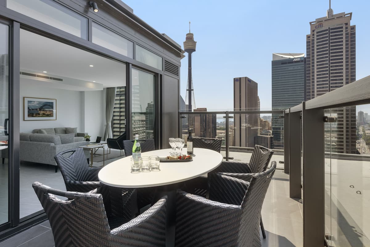 Una terraza moderna en la azotea con una mesa redonda, sillas de mimbre y barandilla de cristal.