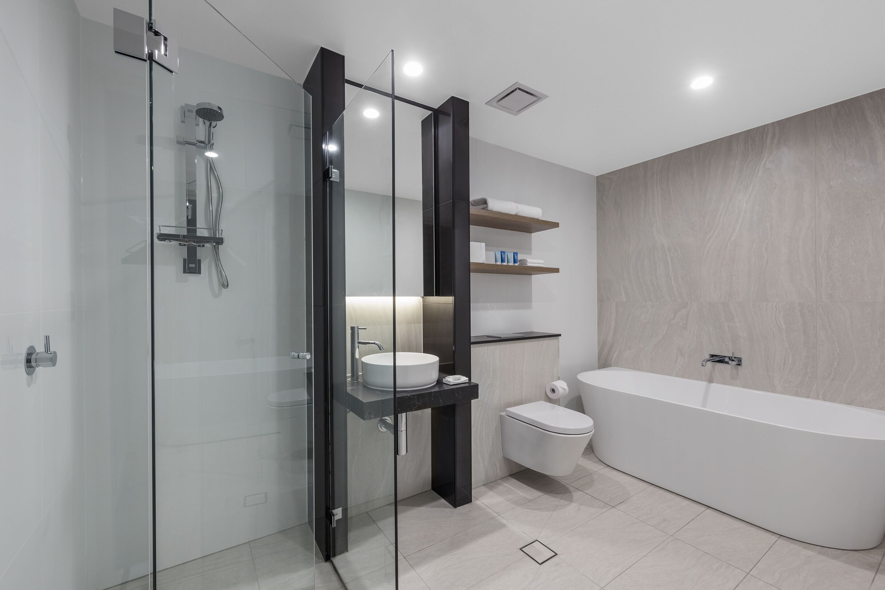 A modern bathroom with a glass-enclosed shower, a freestanding bathtub, a toilet, and a vanity with a sink and shelves.