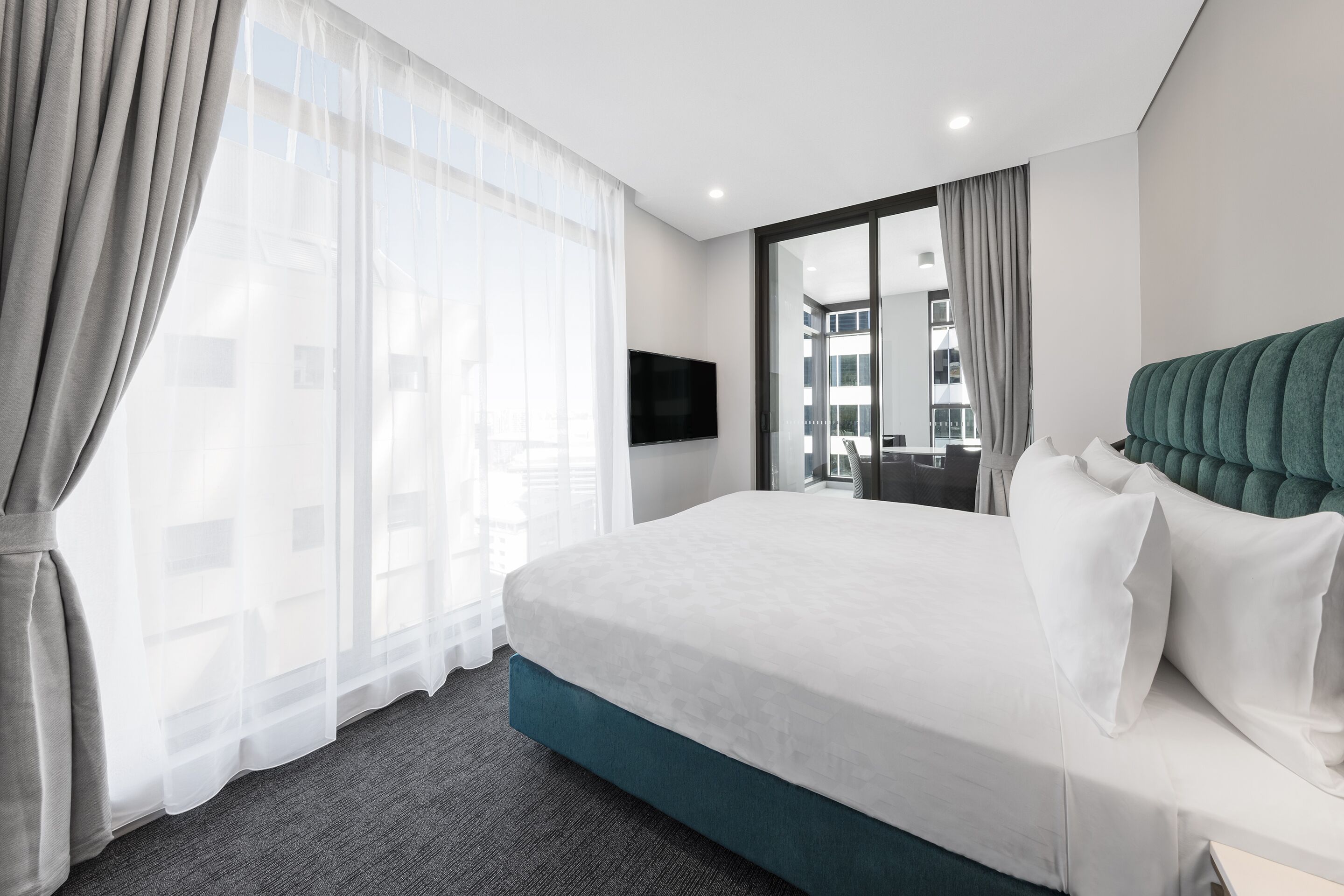 Habitación de hotel moderna con una cama grande, televisor de pantalla plana y vistas de la ciudad a través de amplias ventanas.