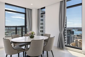 Een moderne eetruimte met een ronde tafel, zes stoelen, grote ramen met gordijnen en uitzicht op de stad.