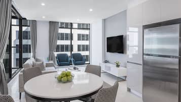 Una sala de estar moderna con una mesa de comedor redonda, sillas azules, un sofá y un televisor grande.