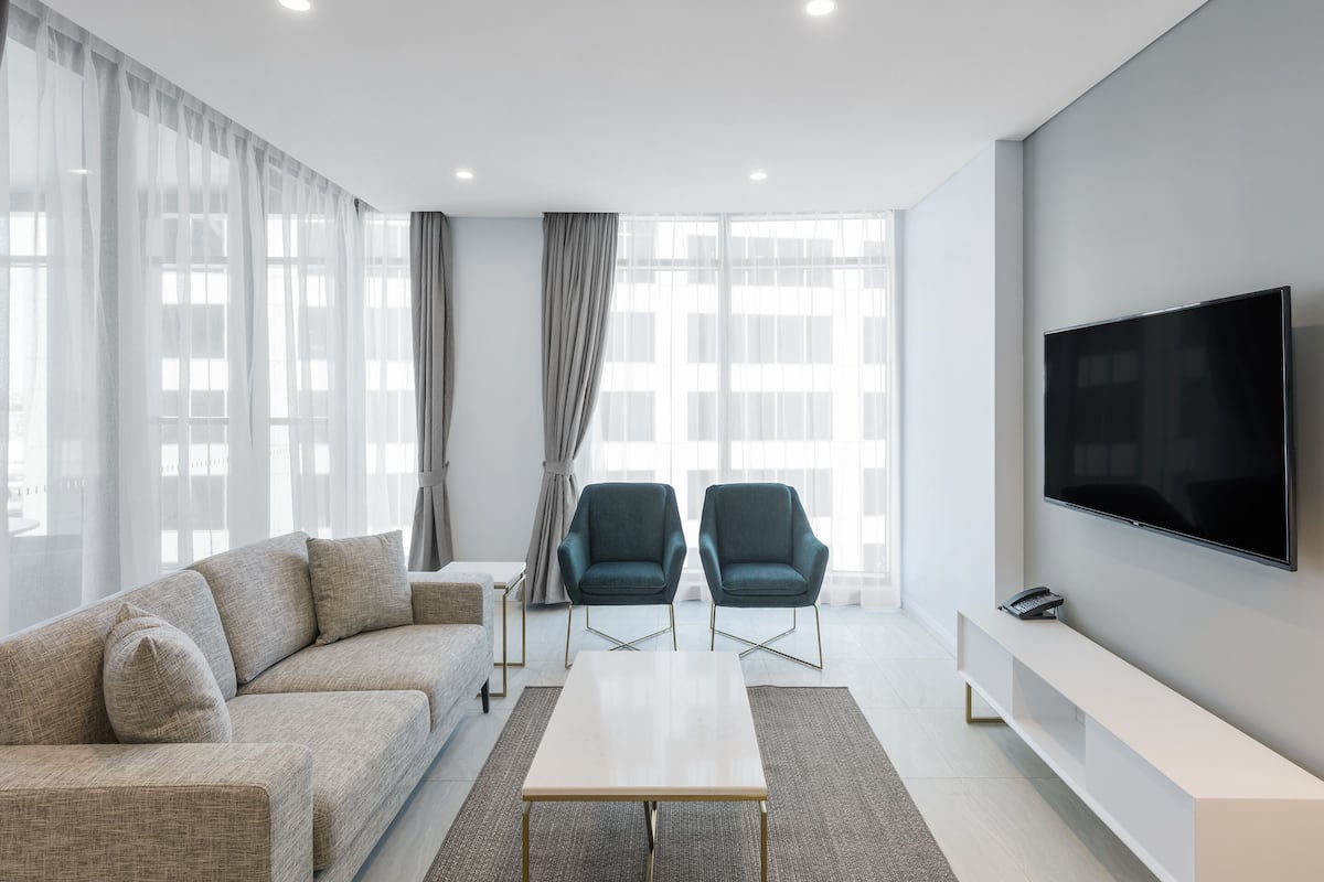 Una sala de estar moderna con un sofá, dos sillones, una mesa de centro, un televisor y un banco.