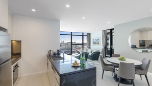 Cucina moderna con isola centrale, zona pranzo con sedie e un'ampia finestra vista città.
