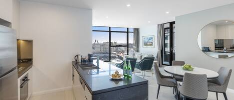 A modern kitchen with a central island, dining area with chairs, and a large window offering a city view.