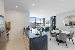 Cozinha moderna com ilha central, área de jantar com cadeiras e uma janela ampla com vista para a cidade.
