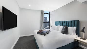A hotel room with a large bed, a flat-screen TV, a window with a city view, and a bedside table with a lamp.