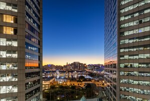 Um edifício alto com vários andares, janelas amplas e vista para o horizonte urbano ao entardecer.