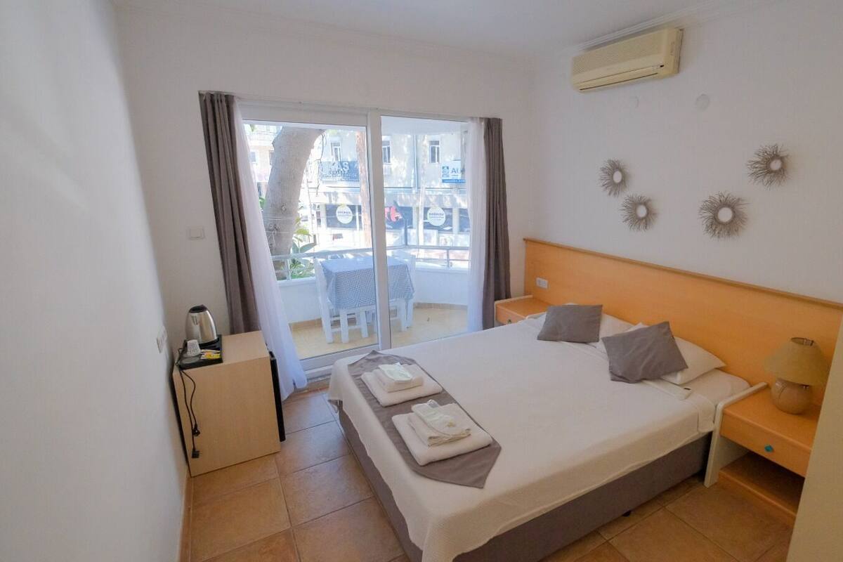 Habitación de hotel con cama, mesita de noche, escritorio con lámpara y vista a la calle a través de una puerta corrediza.