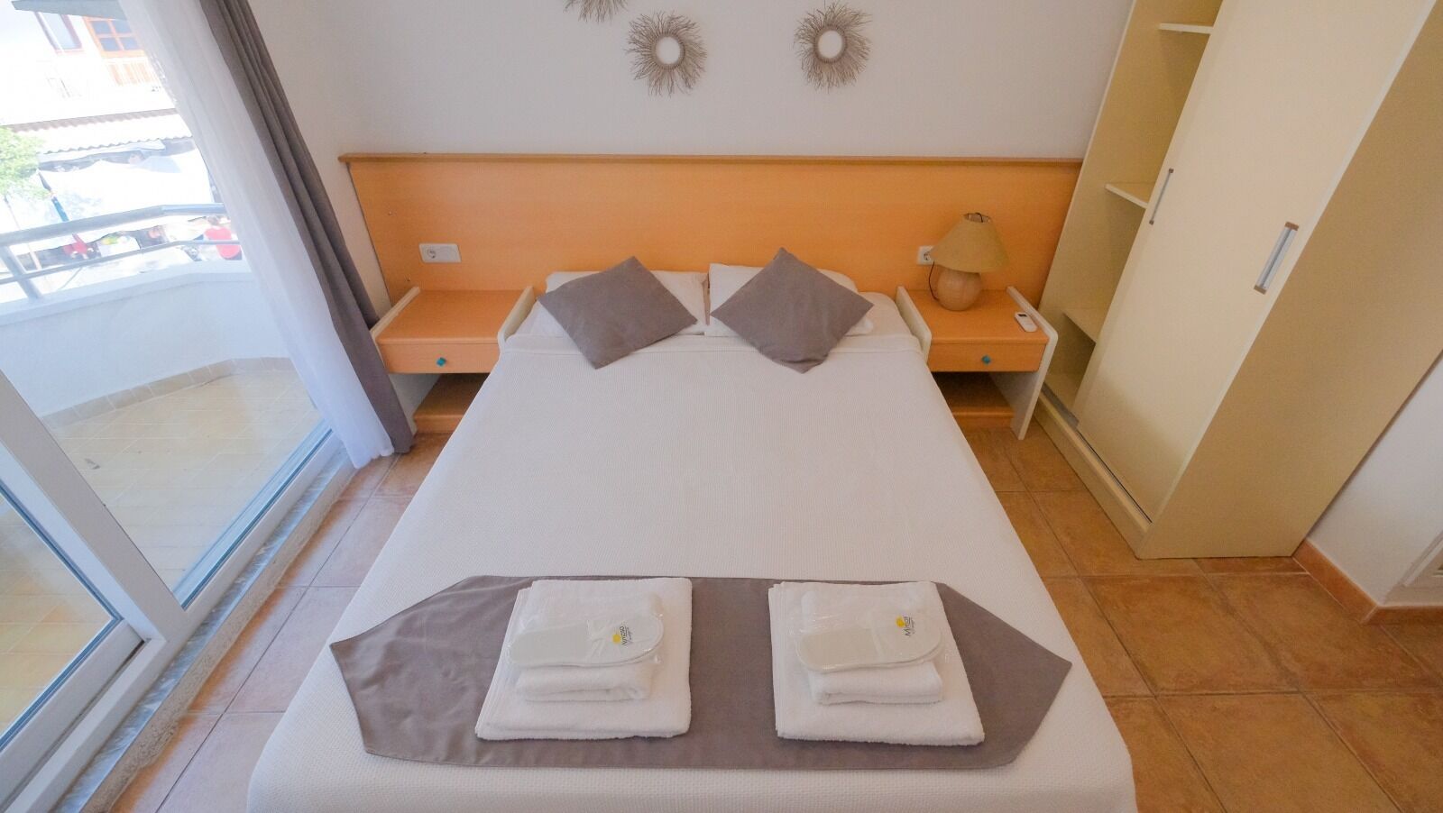 A hotel room with a bed, two pillows, a nightstand, a lamp, and a wardrobe.