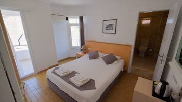 A hotel room with a bed, a bedside table, a lamp, a picture on the wall, and a bathroom door.