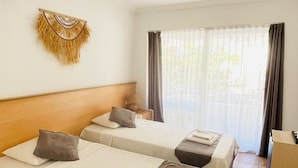 A hotel room with two beds, a wall-mounted air conditioner, a decorative wall hanging, and a window with curtains. - Mimosa Pension (Kas)
