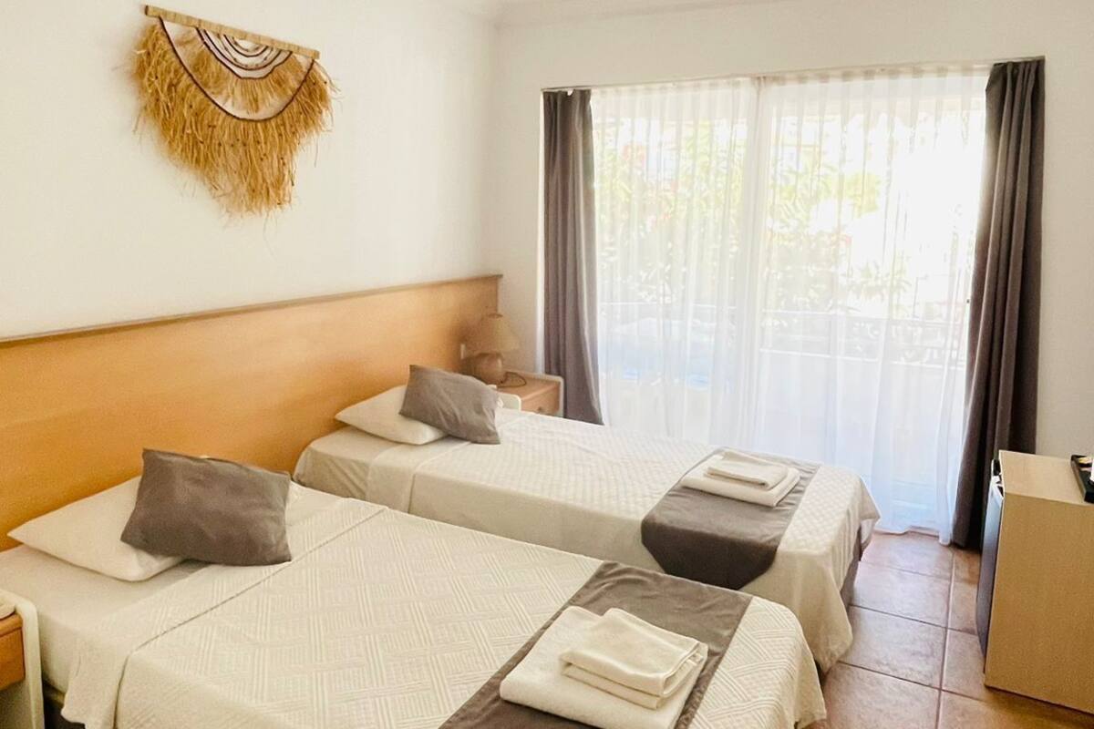 Habitación de hotel con dos camas, aire acondicionado de pared, un adorno en la pared y una ventana con cortinas.
