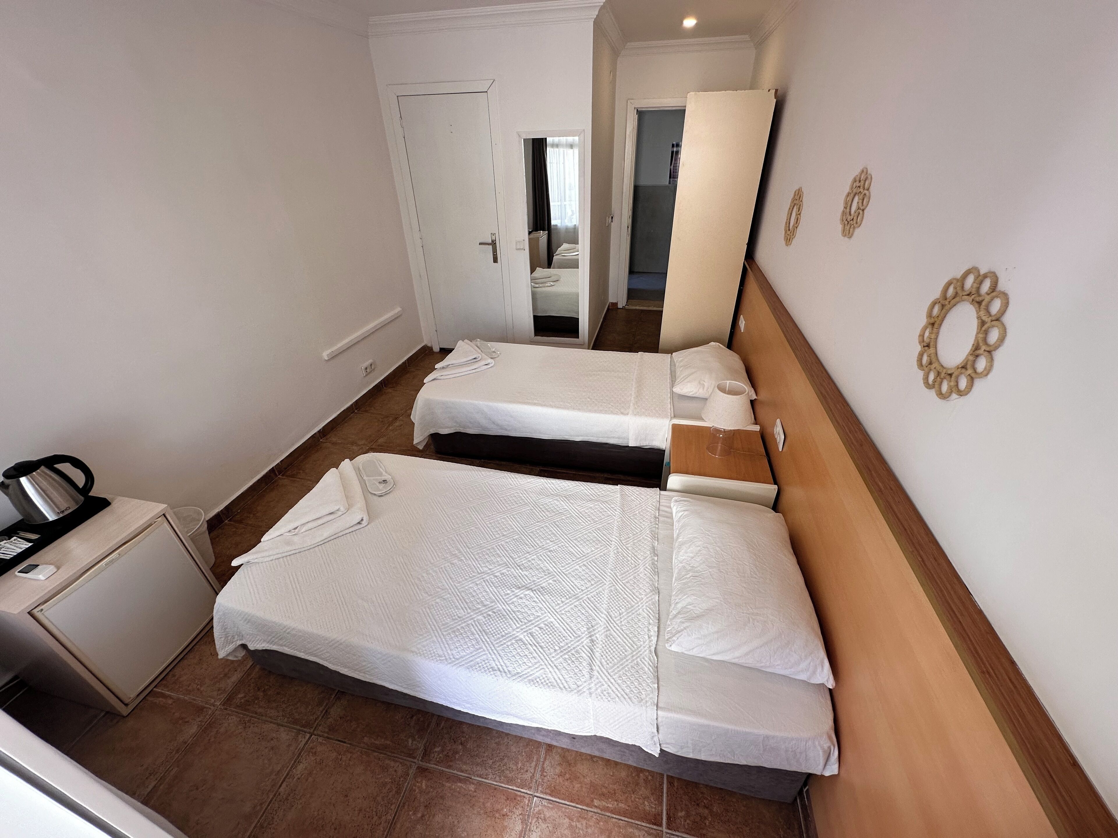 A hotel room with two beds, a small desk with a kettle, and a door leading to another room.