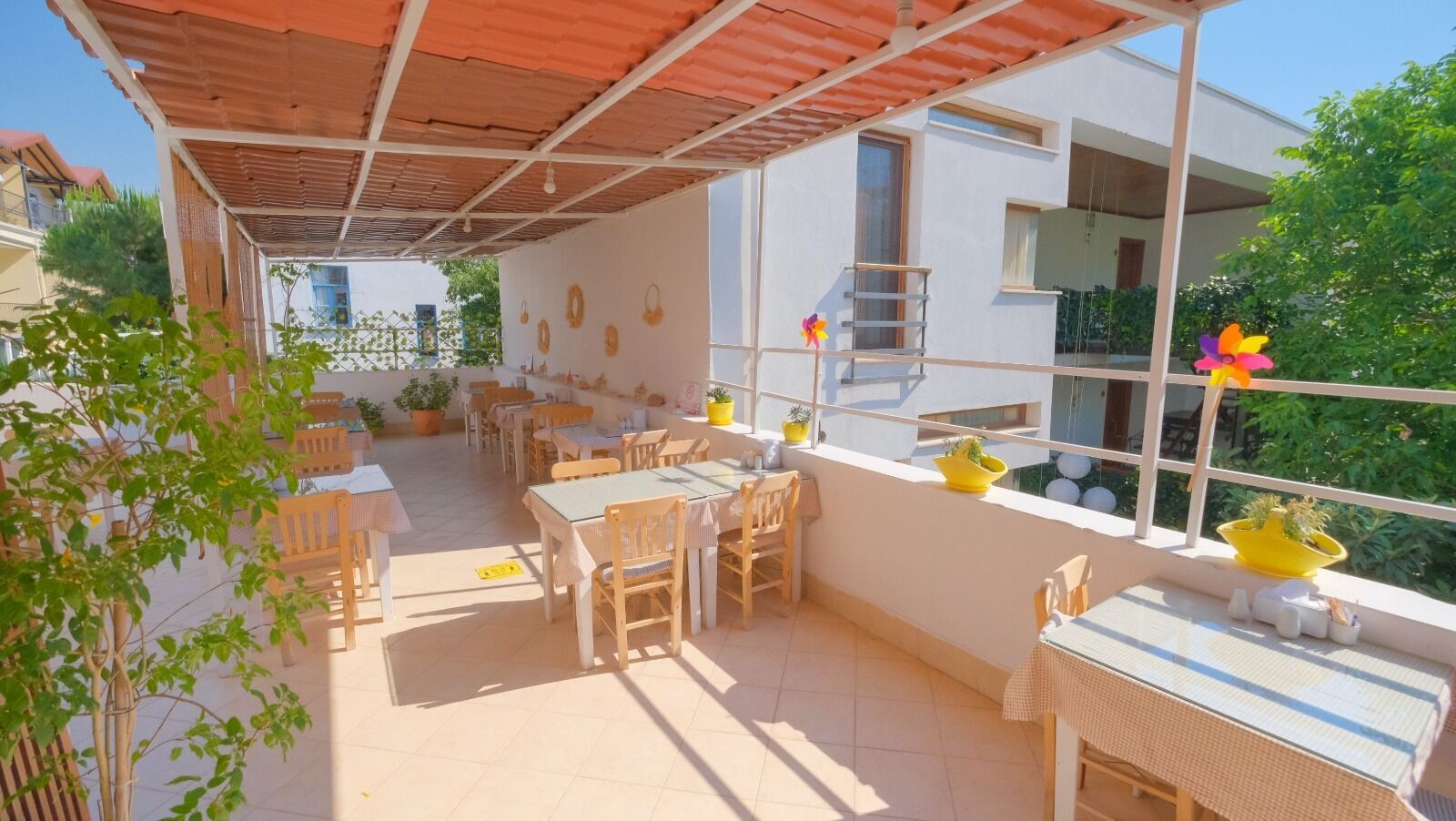 A covered outdoor patio with tables and chairs, potted plants, and a view of a building.