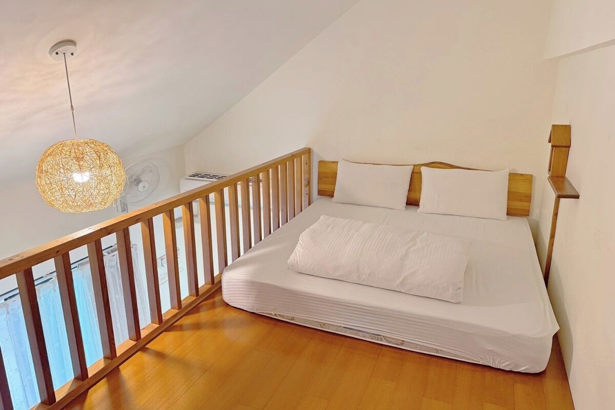 A bedroom with a wooden bed, white bedding, a wooden railing, and a hanging light fixture.