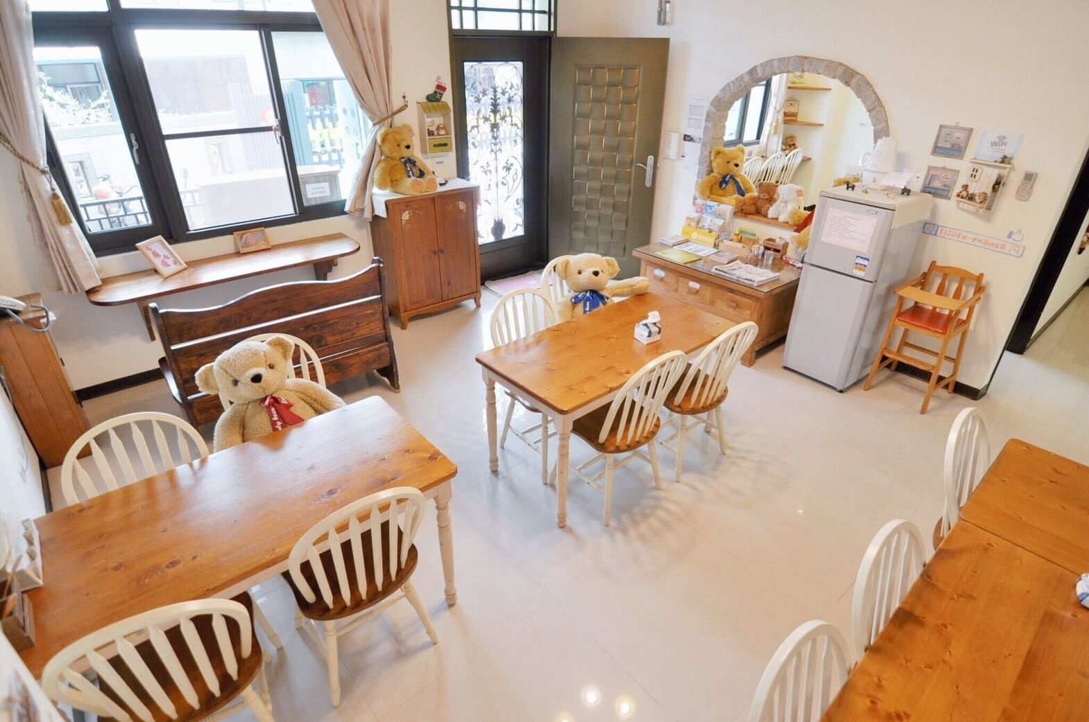 Un comedor acogedor con una mesa de madera y sillas blancas, un oso de peluche sobre la mesa y un refrigerador al fondo.