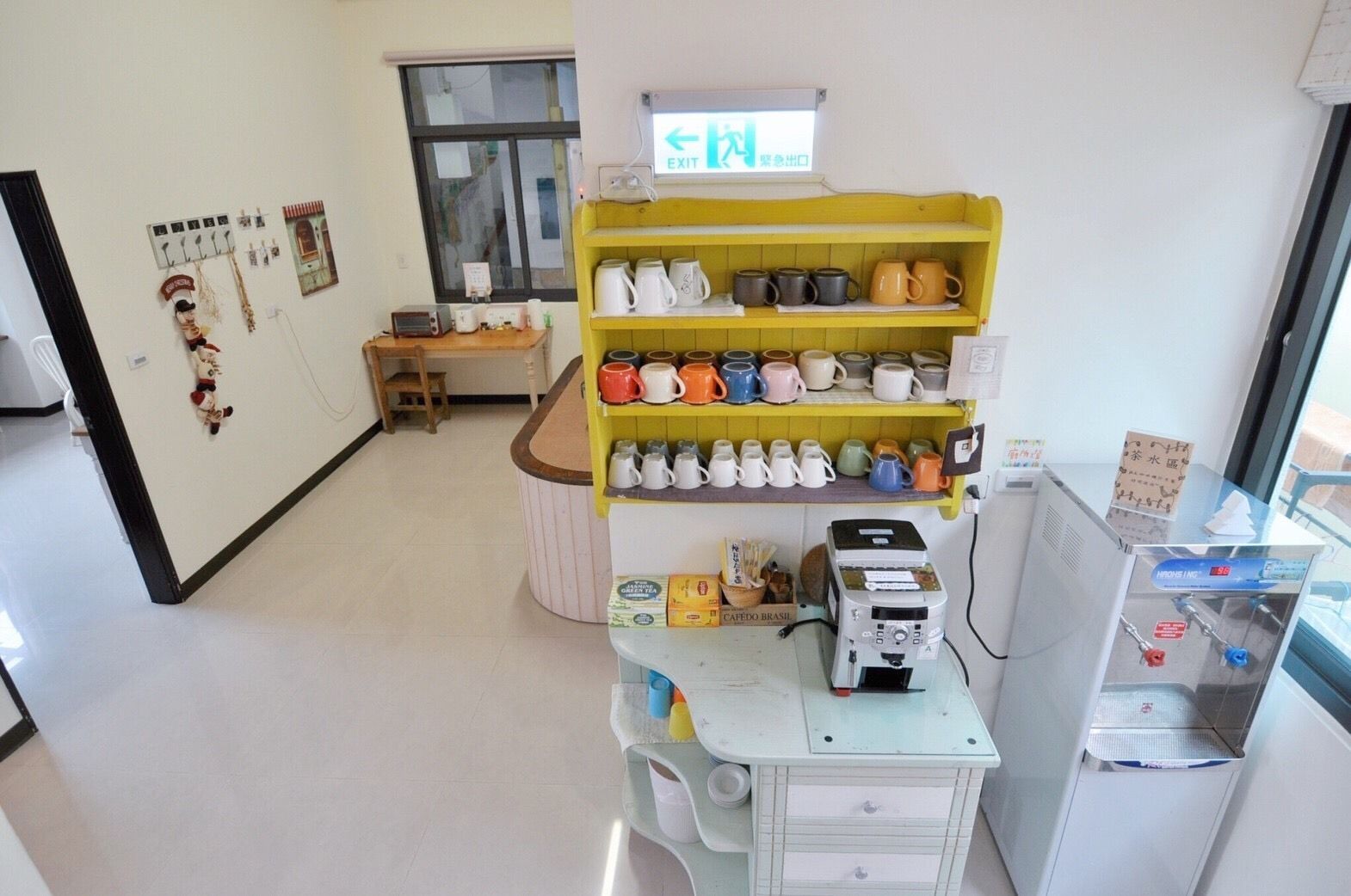 A kitchen area with a coffee machine, a shelf with various mugs, and a sign indicating an exit.