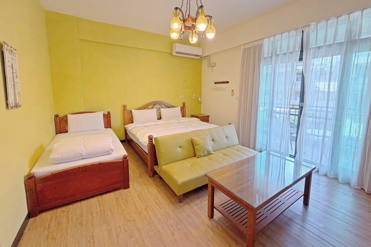 A room with two beds, a sofa, a wooden table, and a chandelier.