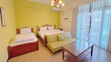 A room with two beds, a sofa, a wooden table, and a chandelier.