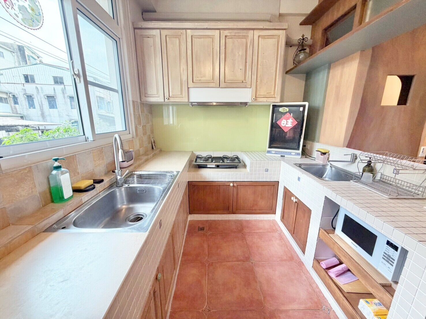A compact kitchen with a gas stove, two sinks, wooden cabinets, and a window.