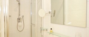 A shower with a handheld showerhead, a glass shelf with toiletries, and a mirror above the sink. - A Place Like Home - Lovely Flat in Pimlico Area (London)