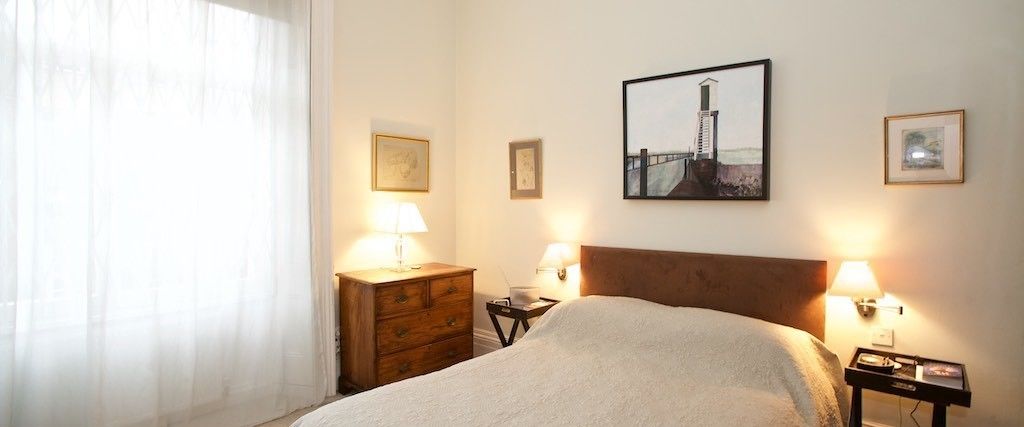A hotel room with a bed, two bedside tables with lamps, a wooden dresser, and framed pictures on the walls.
