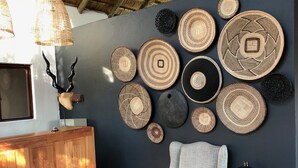 A room with a wooden reception desk, a patterned rug, a grey armchair, and a wall adorned with woven decorative plates. - Ku Sungula Safari Lodge (Hoedspruit)