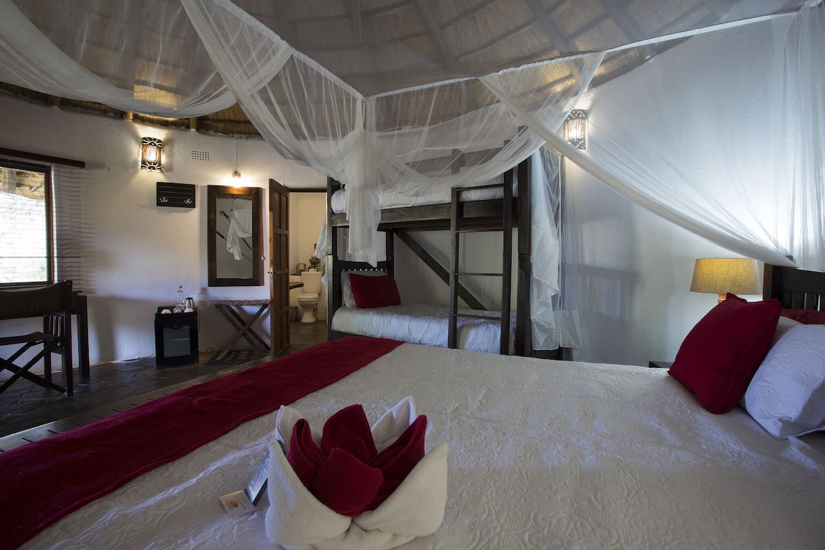 A bedroom with a bed, a red throw blanket, and a white canopy.