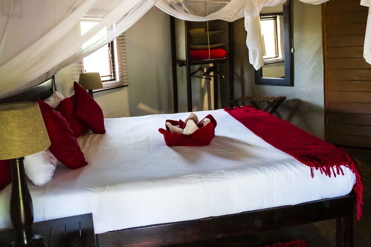 A bed with a canopy, red pillows, and a red throw blanket.