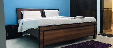 A bedroom with a bed, a nightstand, a wardrobe, and a purple rug.