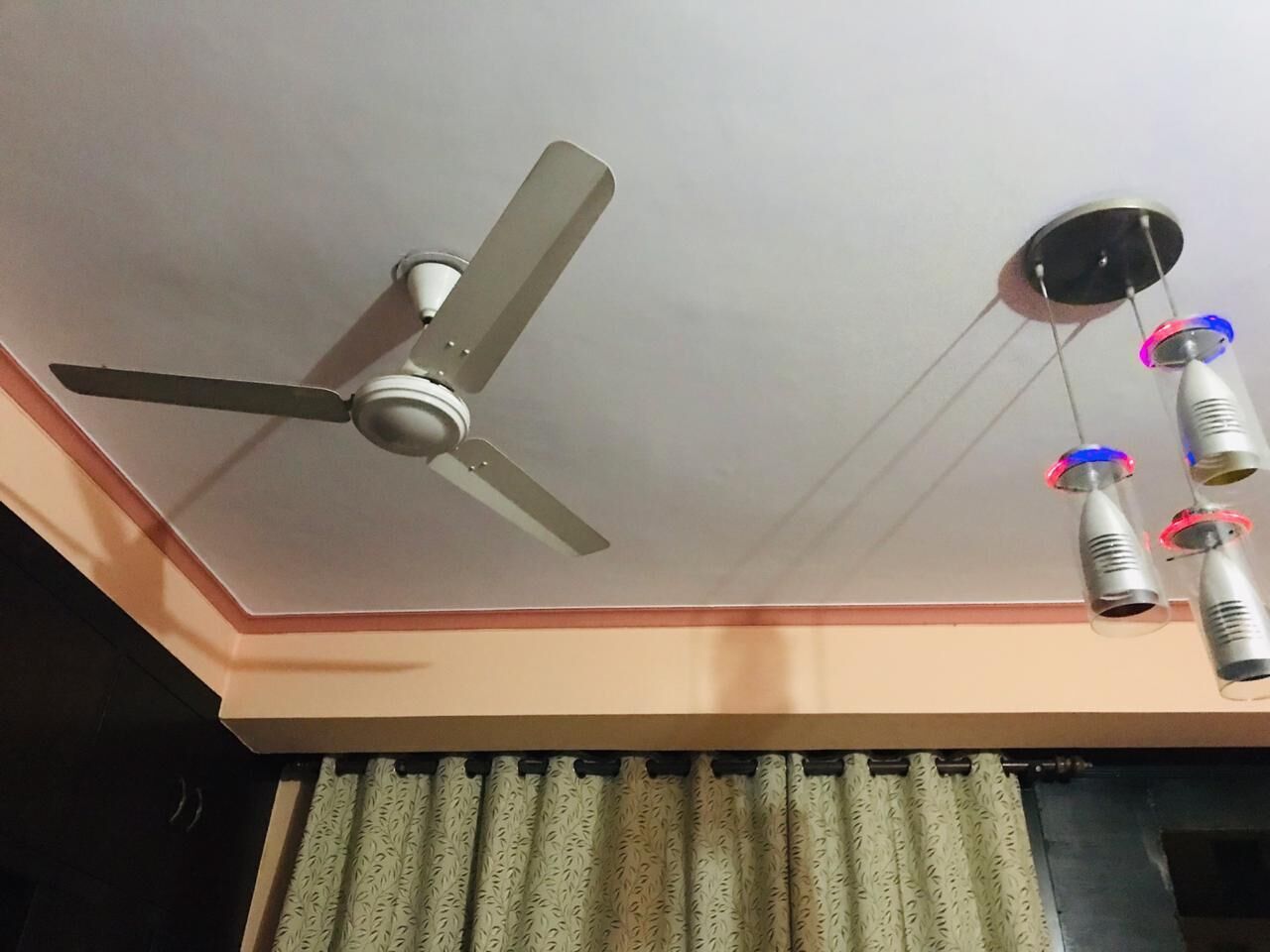En ventilator i loftet, en pendel med rund bund og en gardinstang med mønstrede gardiner.