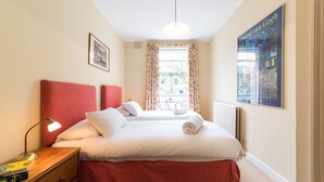 Ein Hotelzimmer mit Bett, Nachttisch, Lampe, einem Bild und einem Fenster mit Vorhängen.