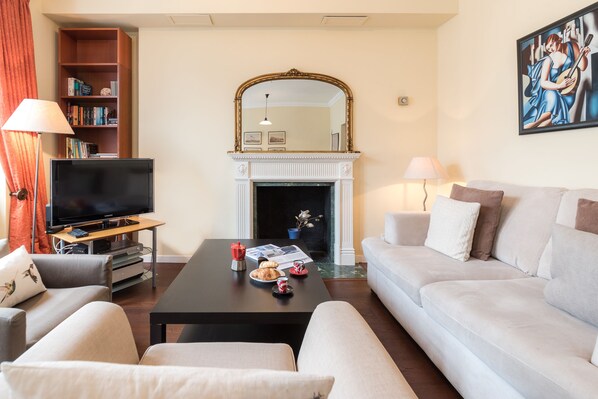 A living room with a television, sofa, coffee table, fireplace, bookshelf, and artwork.