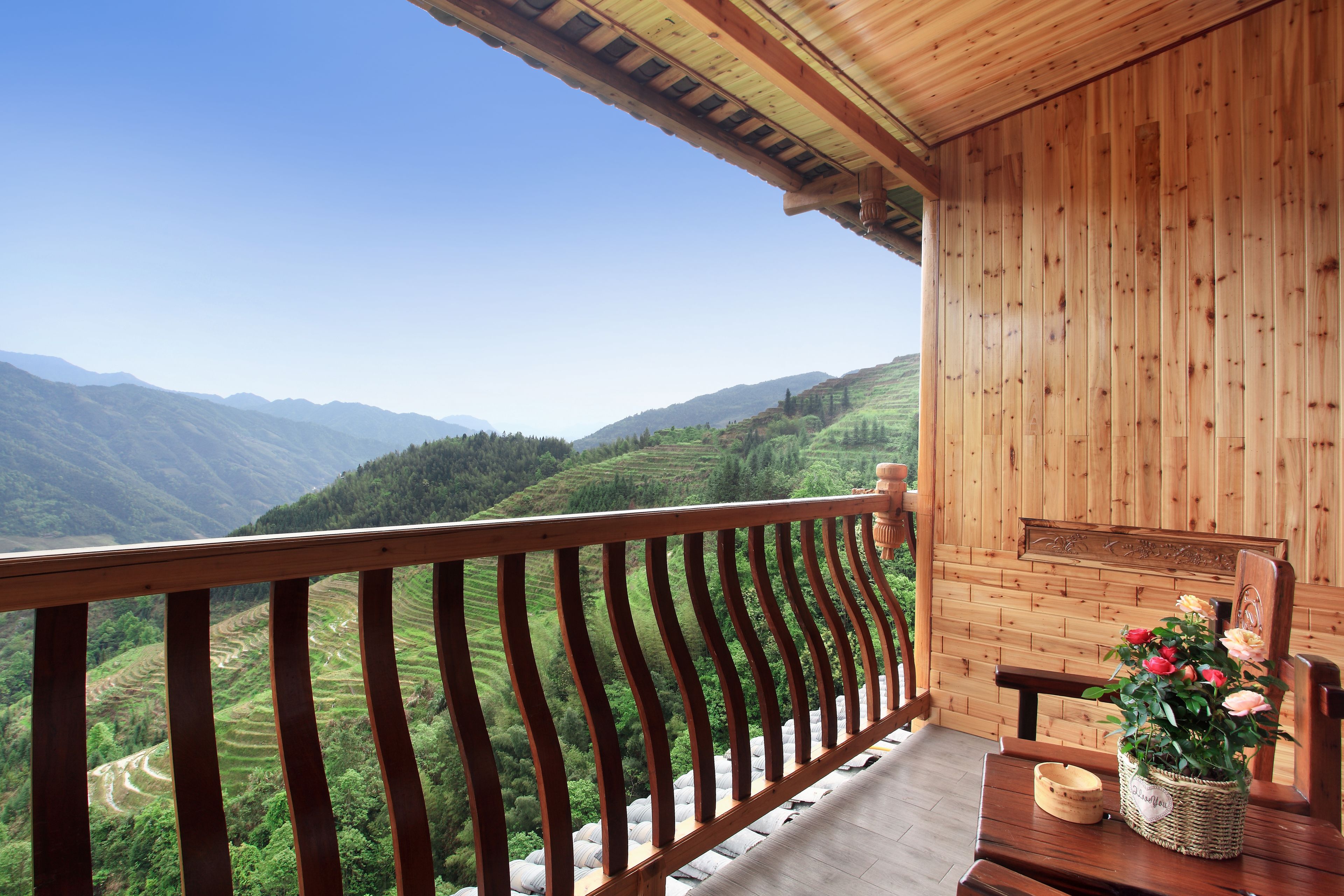 Un balcón de madera con vistas a campos escalonados y montañas.