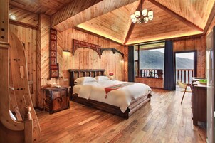 A wooden-themed bedroom with a large bed, a nightstand, and a view of mountains through a balcony.