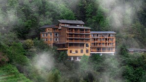 Un bâtiment en bois à plusieurs étages, doté de balcons, entouré d’une forêt dense et enveloppé de brume.