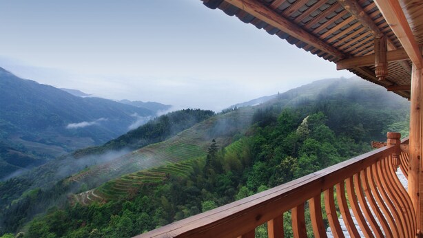 Un balcon en bois donnant sur des champs en terrasses et des montagnes.