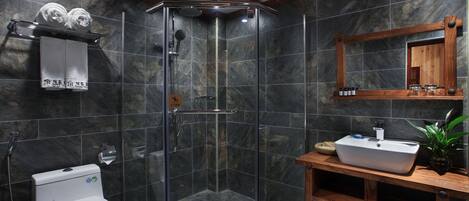 Un baño moderno con ducha envuelta en cristal, inodoro blanco, tocador de madera con lavamanos y espejo sobre el tocador.