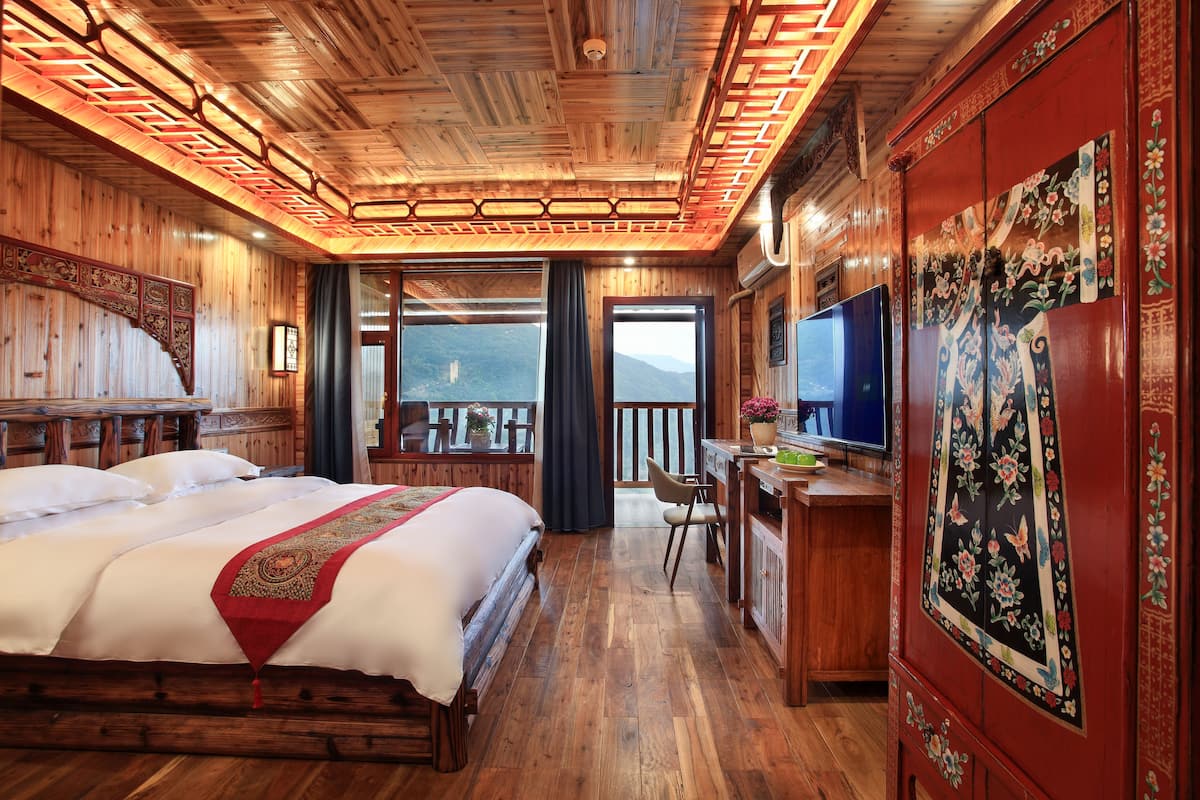 Una habitación de madera con una cama, escritorio, televisor y vistas a las montañas.