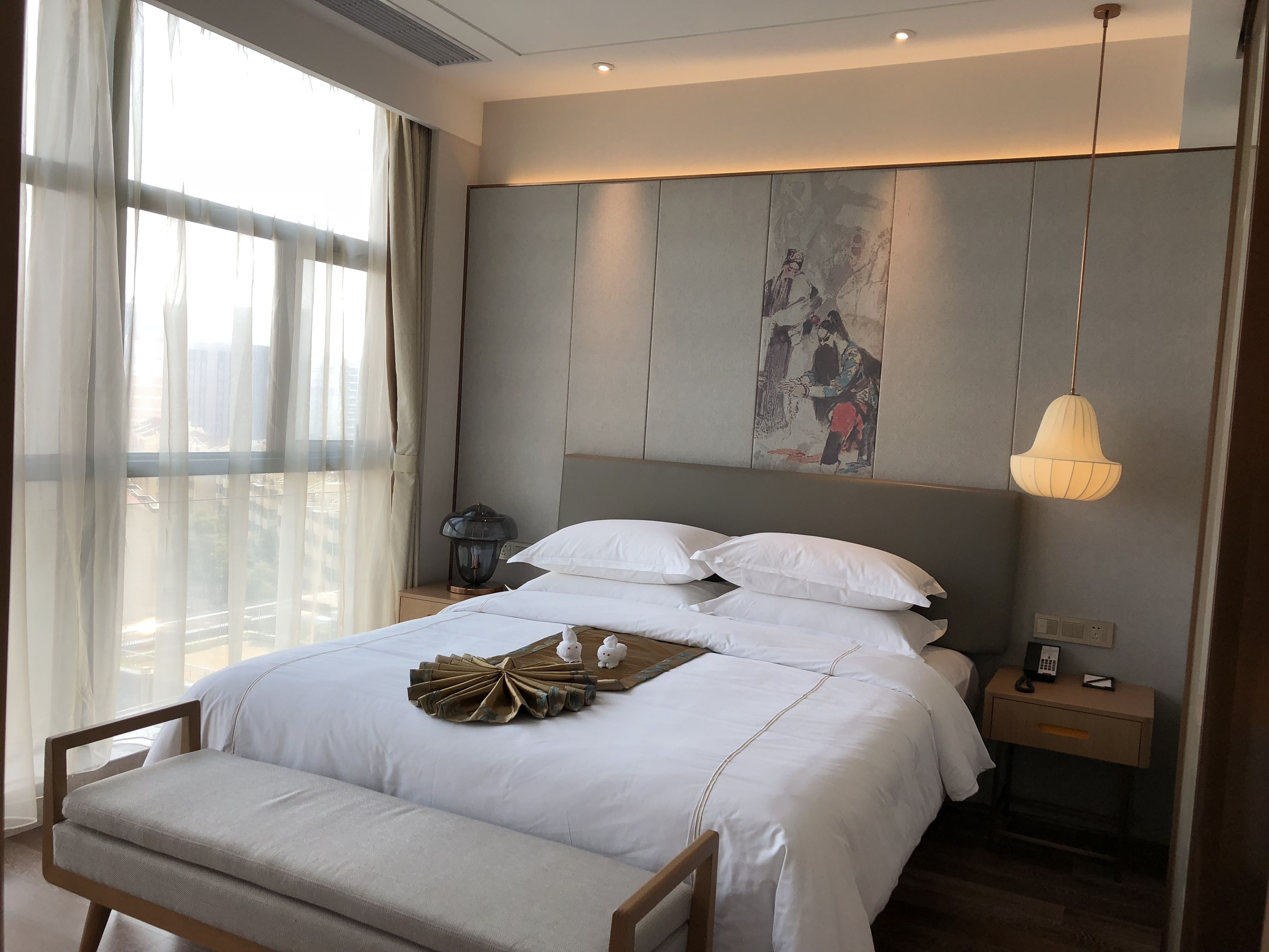 A modern hotel room with a large bed, bedside table, and a wall-mounted artwork.
