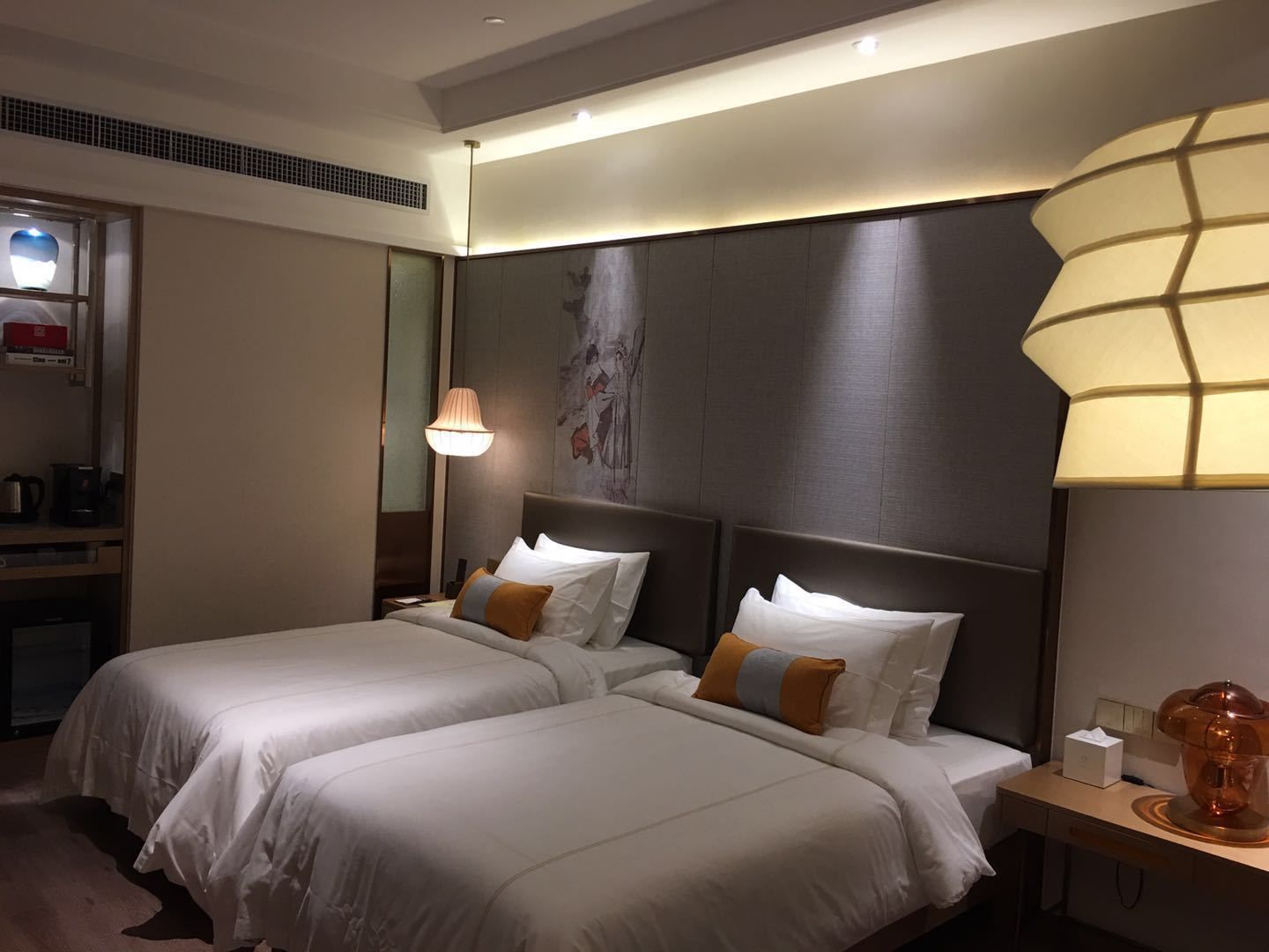 A hotel room with two beds, a nightstand with a lamp, a mirror, and a wall with artwork.