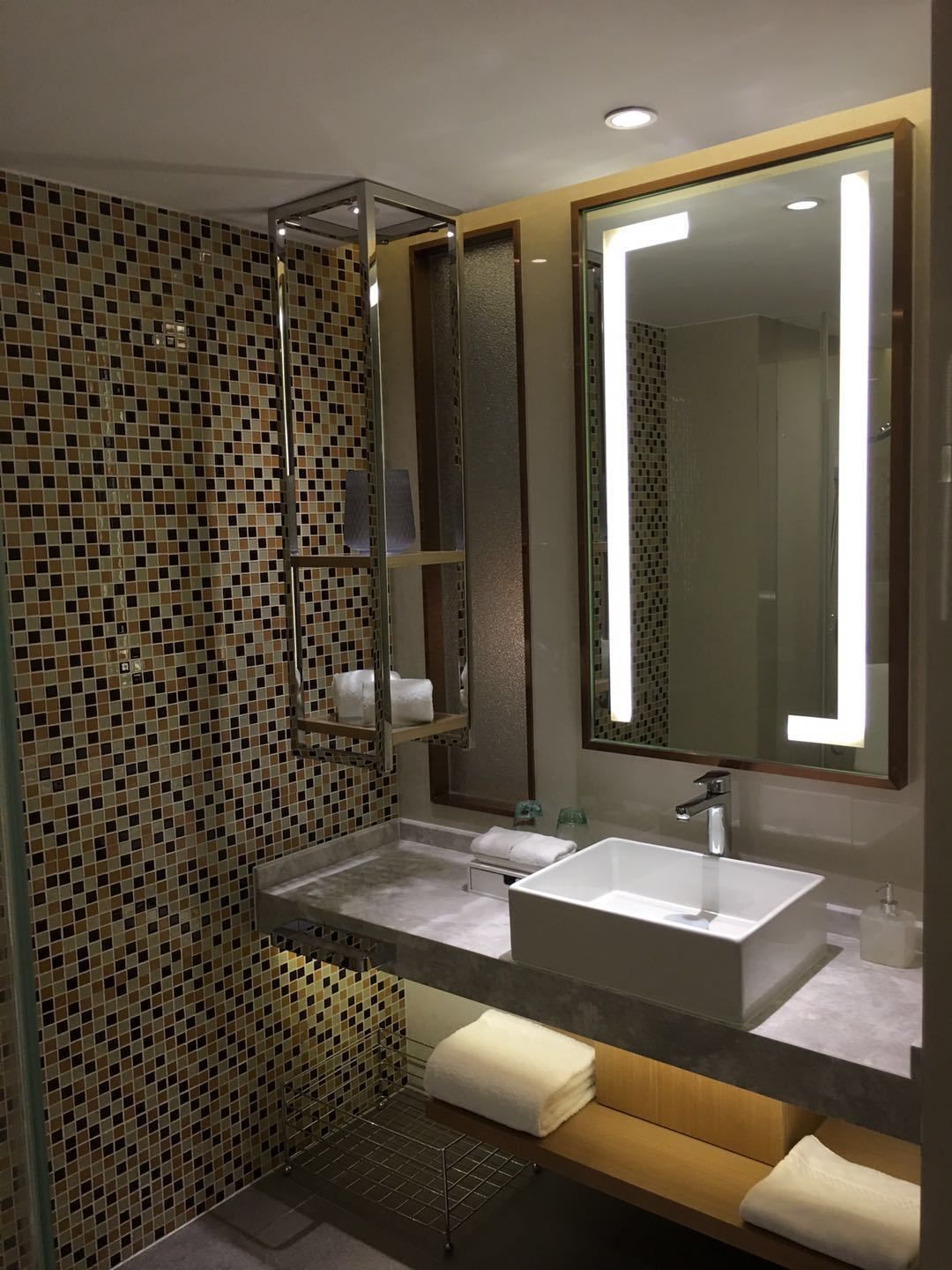 A modern bathroom with a large mirror, two sinks, and a tiled mosaic wall.