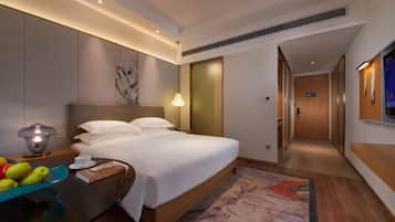 A hotel room with a large bed, a bedside table with a lamp, a fruit bowl, and a painting on the wall.