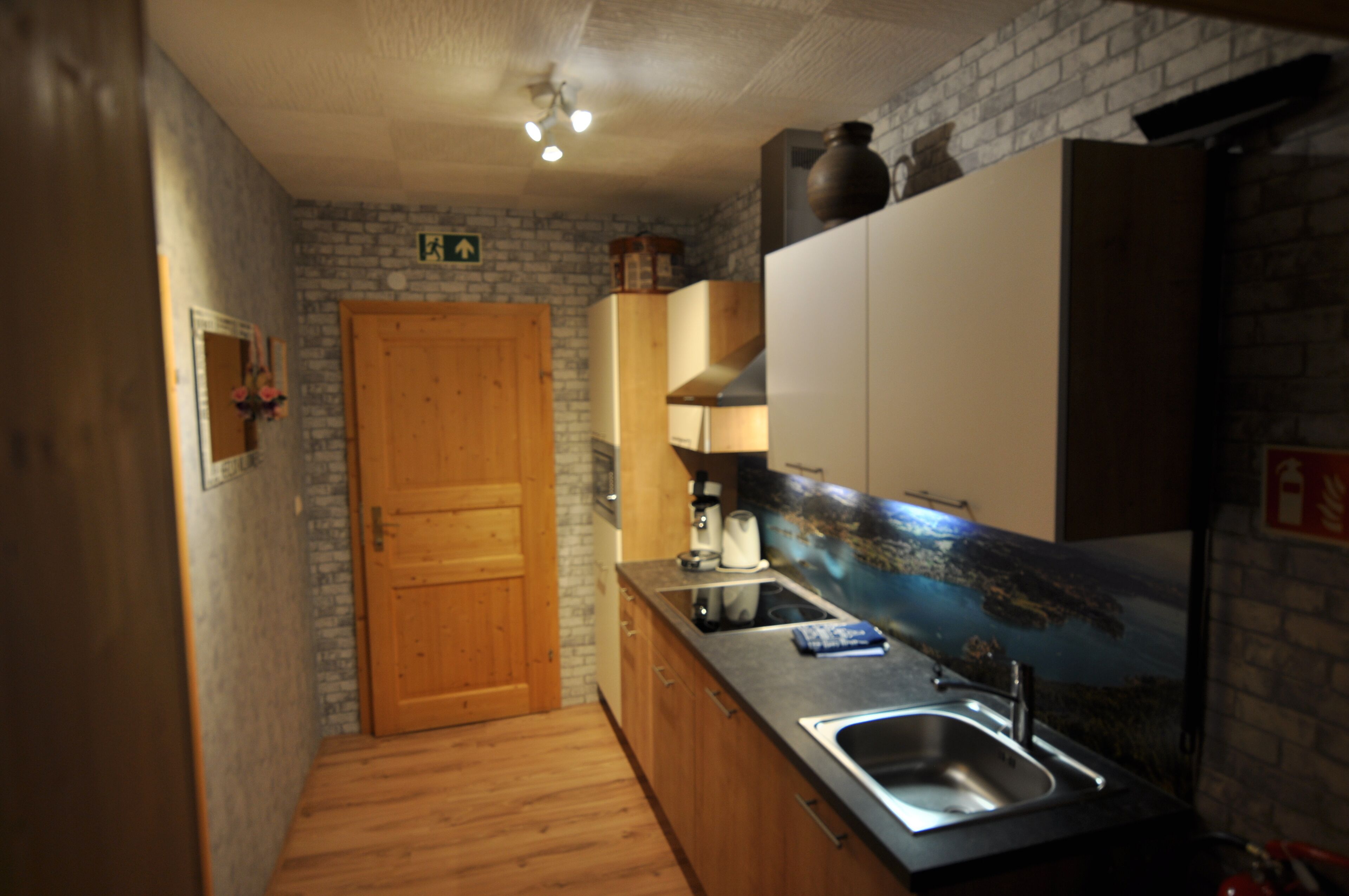 A narrow kitchen with wooden cabinets, a sink, and a stone wall.